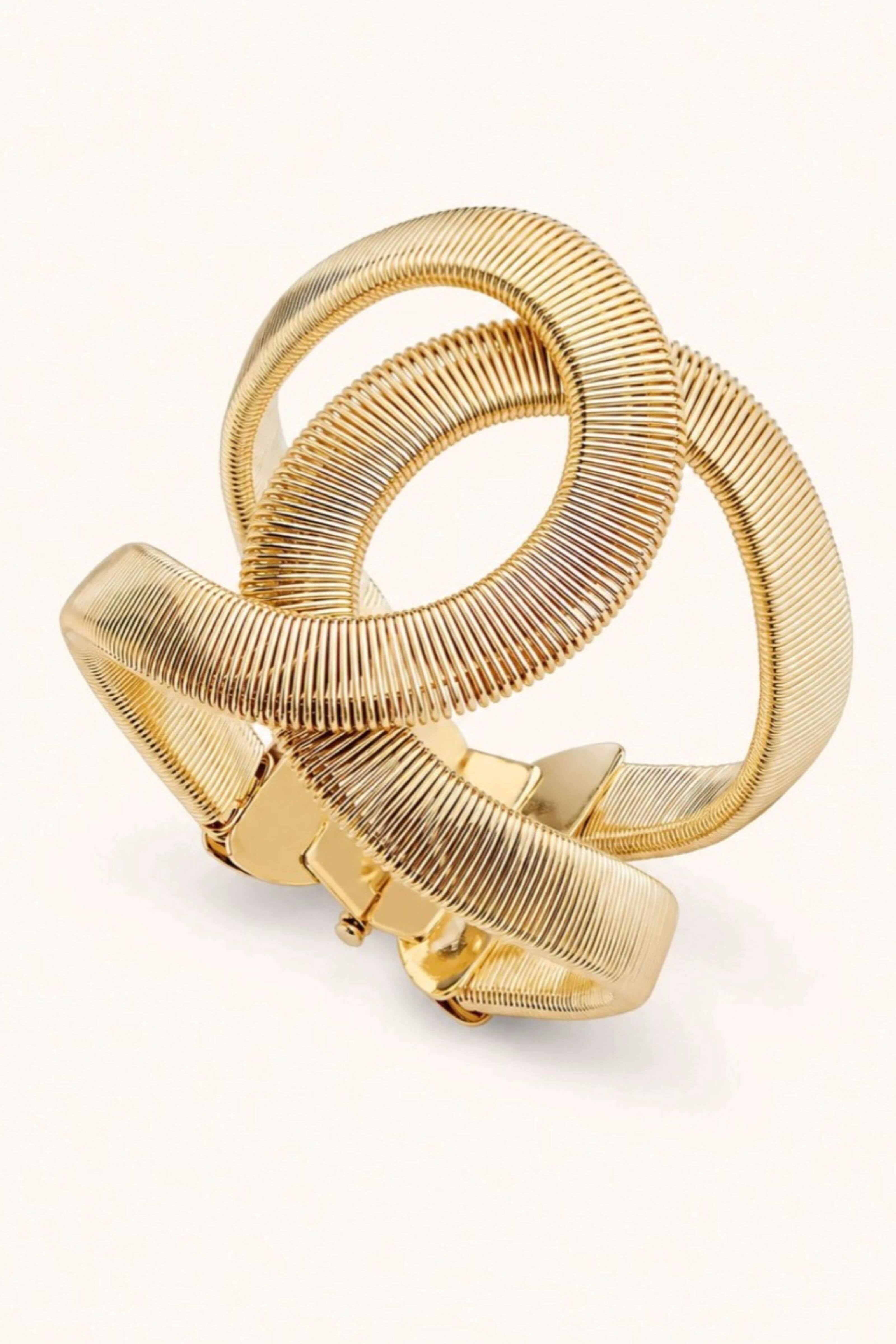A gold-toned metal cuff bracelet with a textured, ribbed snake-skin style design and a buckle closure, shown on a plain white background.