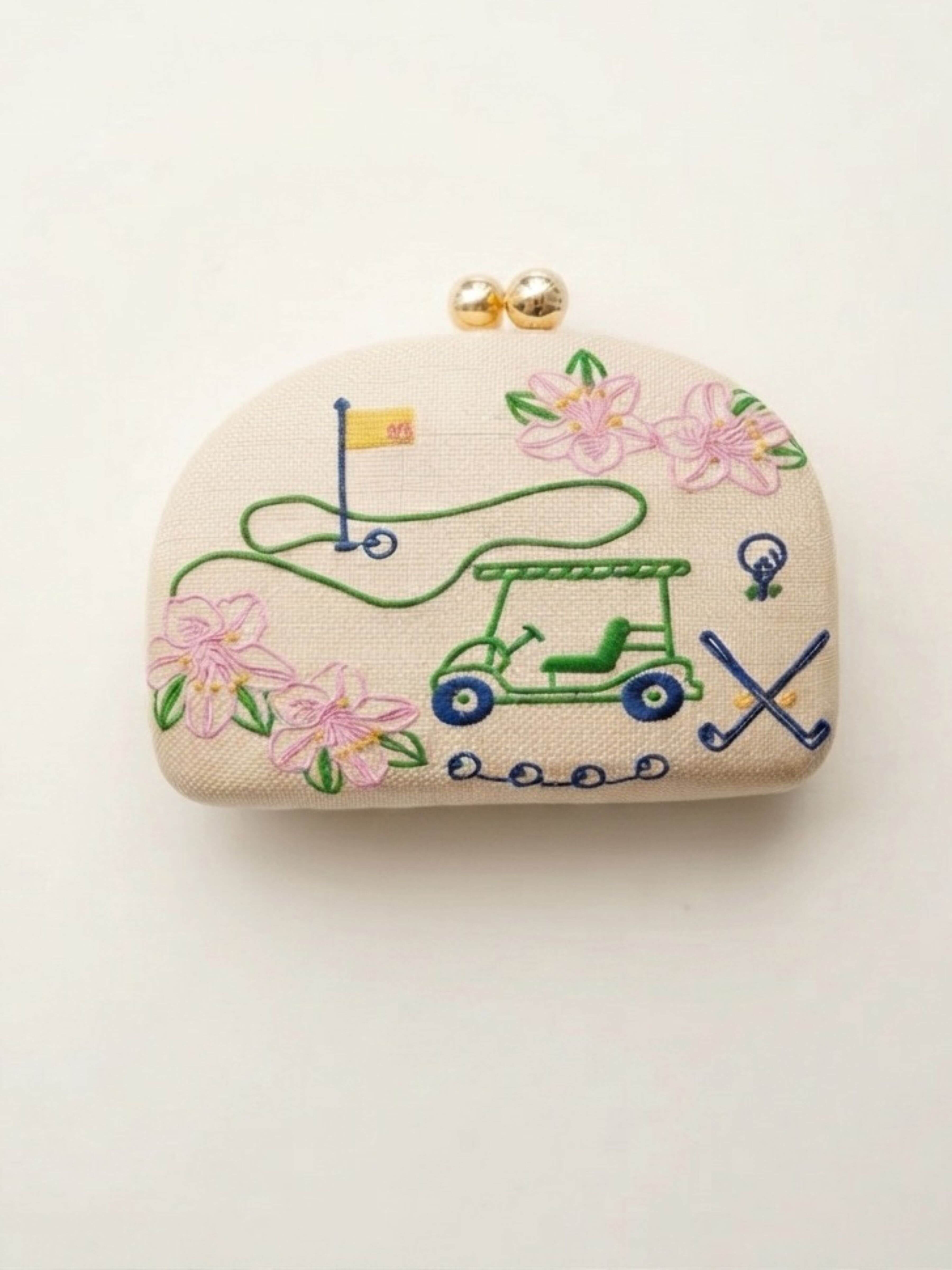 A small beige fabric coin purse with gold-tone clasp hardware, featuring embroidered golf-themed motifs including a green golf cart, pink flowers, a flagstick, and crossed clubs on a plain white background.