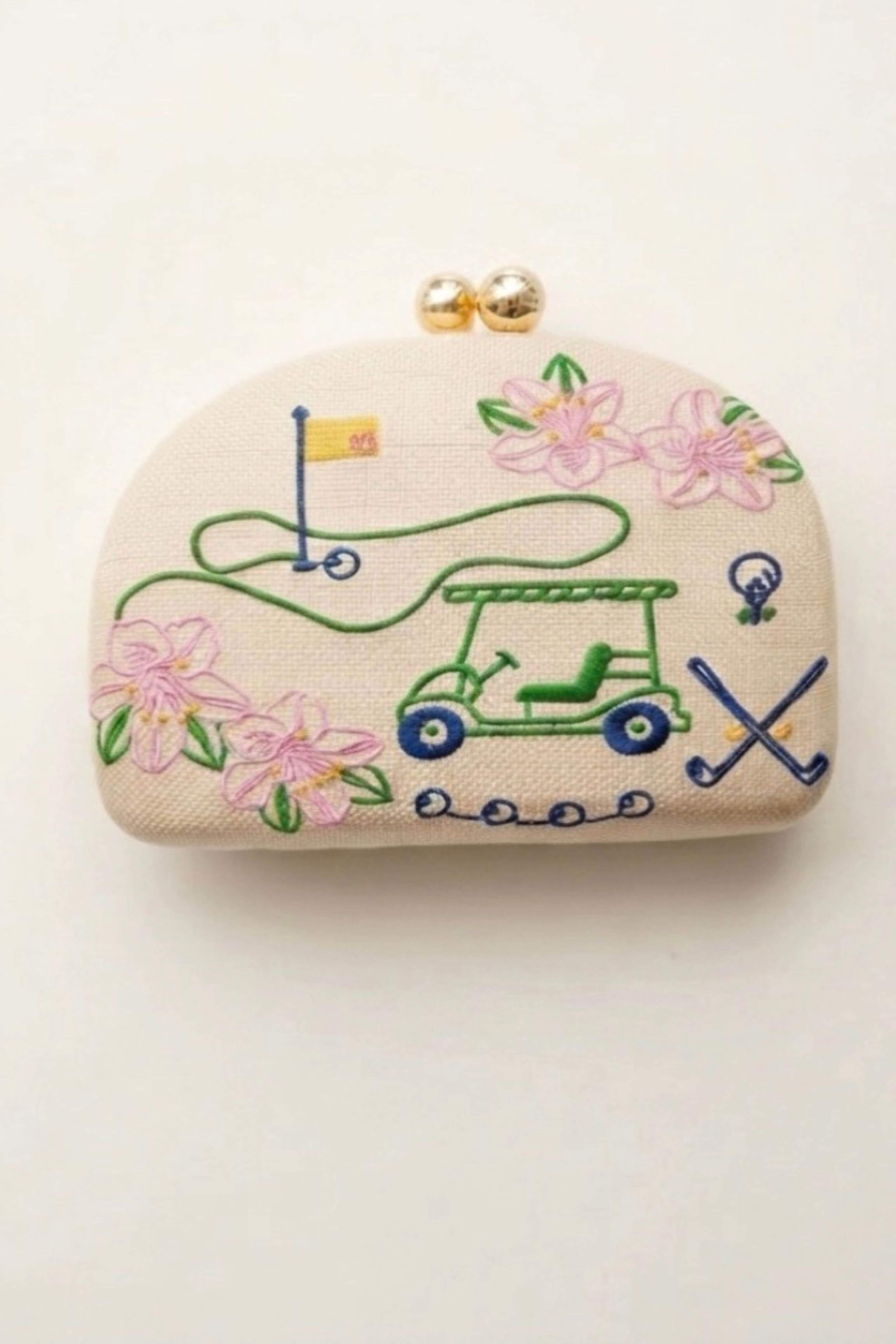 A small beige fabric coin purse with gold-tone clasp hardware, decorated with embroidered golf-themed motifs including a green golf cart, pink flowers, a flagstick, and crossed clubs on a white background.
