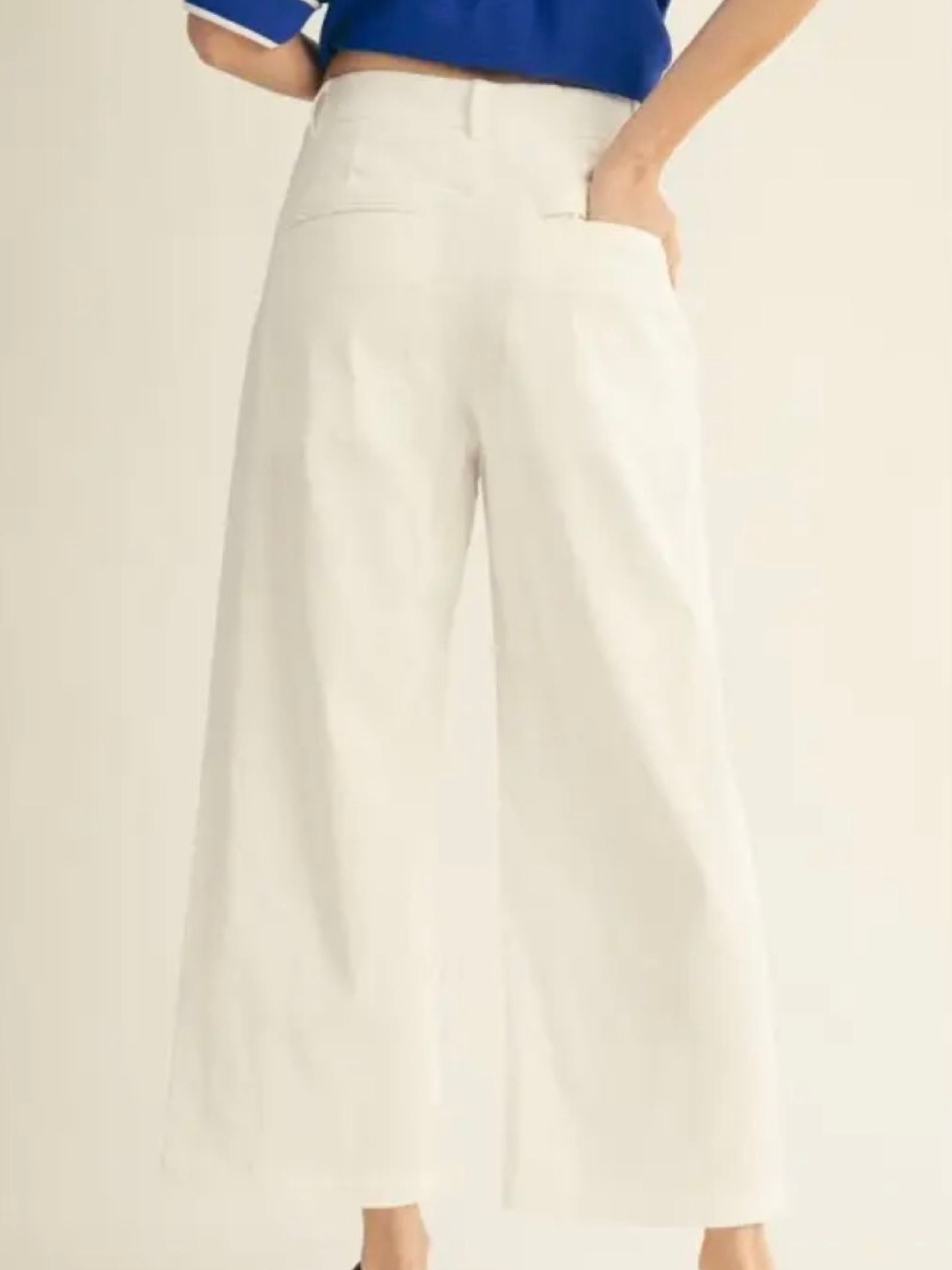 A person wearing high-waisted, wide-leg cropped pants in an off-white or cream color, paired with a blue top. The photo is cropped from the waist down against a plain, light beige studio background.