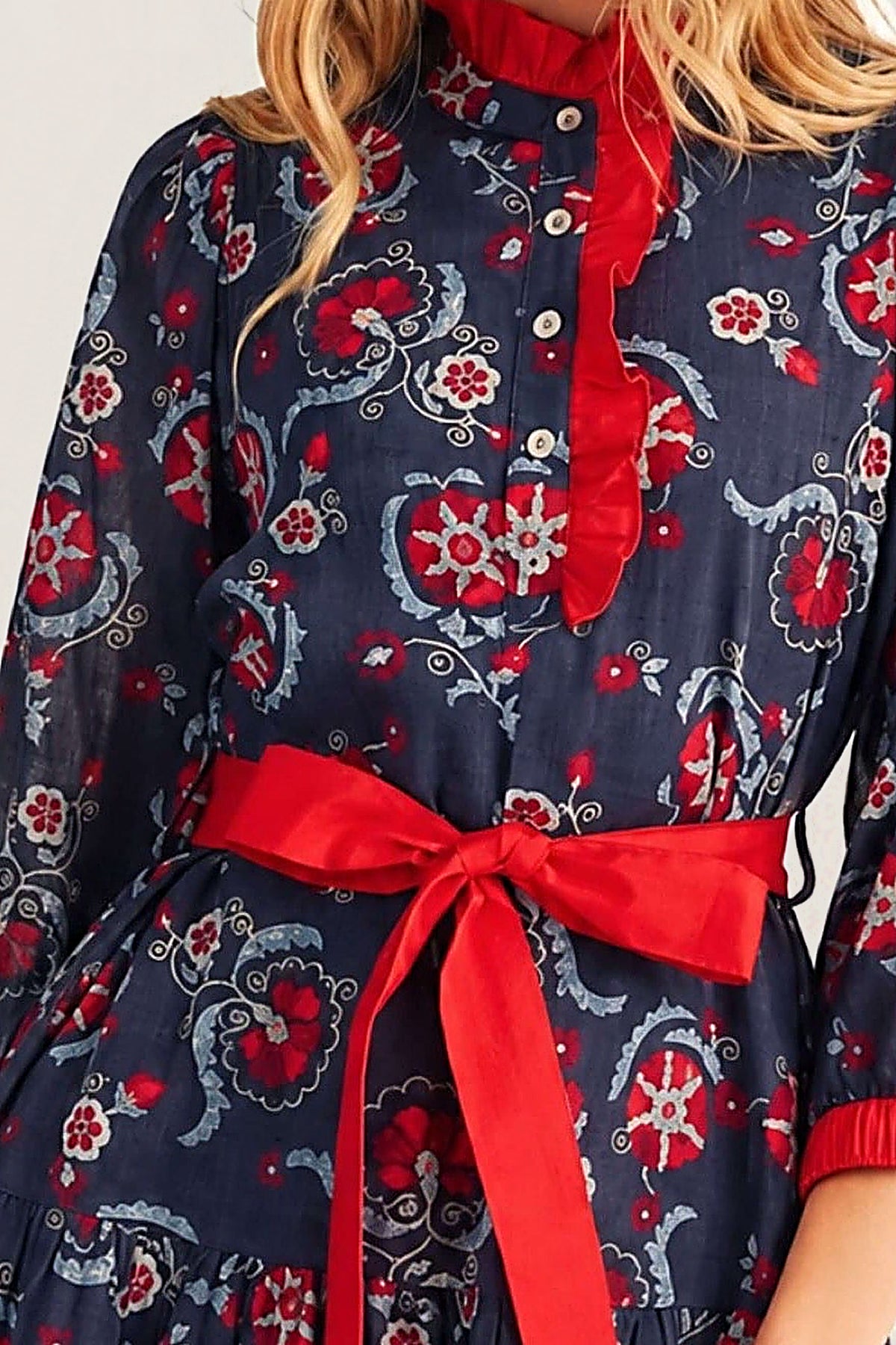 Close-up of the Liberty Blooms Dress showing the red ruffled collar and placket, the navy floral print with red and ivory blooms, and the red self-tie waist bow.