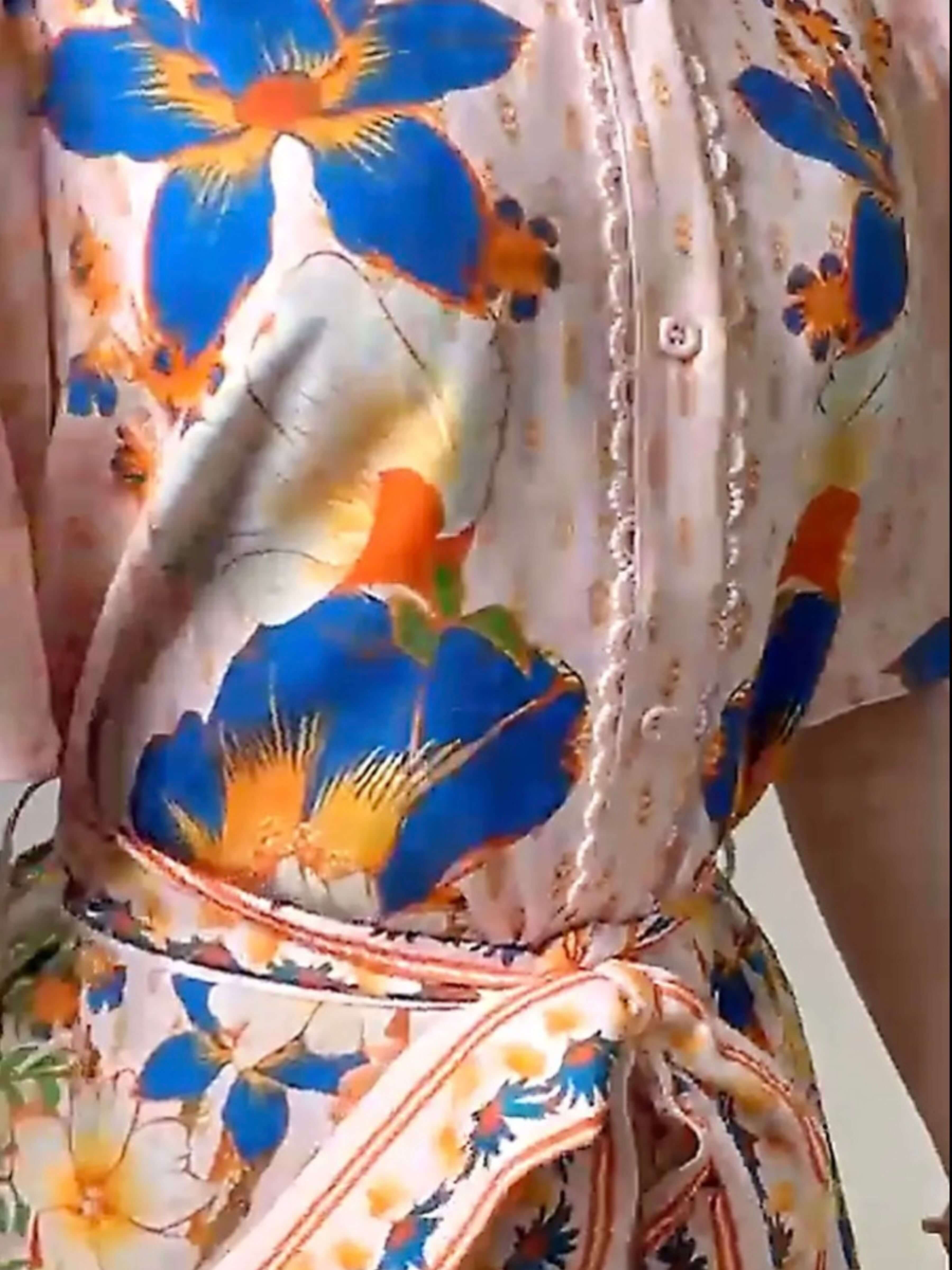 Close-up of a floral dress or robe with a cream base, large blue flowers, orange centers, and a matching tie belt at the waist.