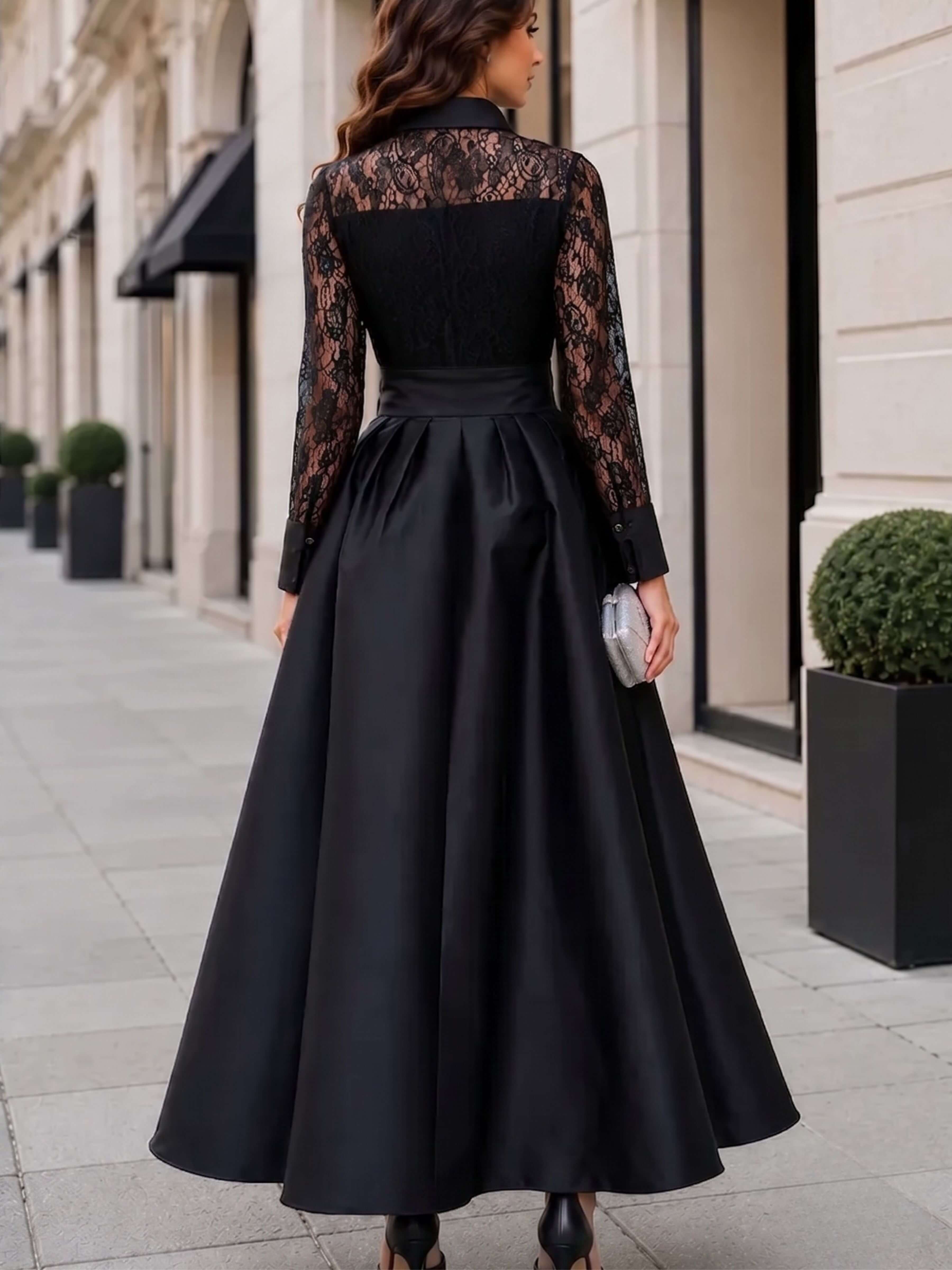 A woman wearing a long black evening gown with sheer black lace long sleeves and a matching black satin waistband, photographed from behind on a city sidewalk.