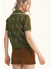 A woman shown from the back wearing a short-sleeve olive green knit sweater with red and gray chevron patterns and a brown mini skirt, against a plain light background.