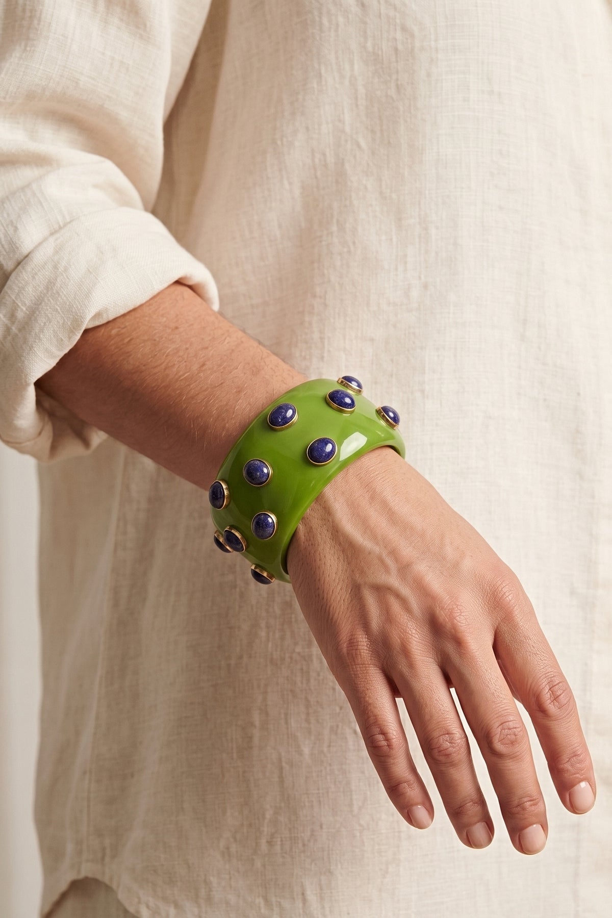 Pea Amethyst Resin Bracelet worn on the wrist with a cream linen shirt, showing how wide the green resin bangle sits and its blue-violet cabochons.