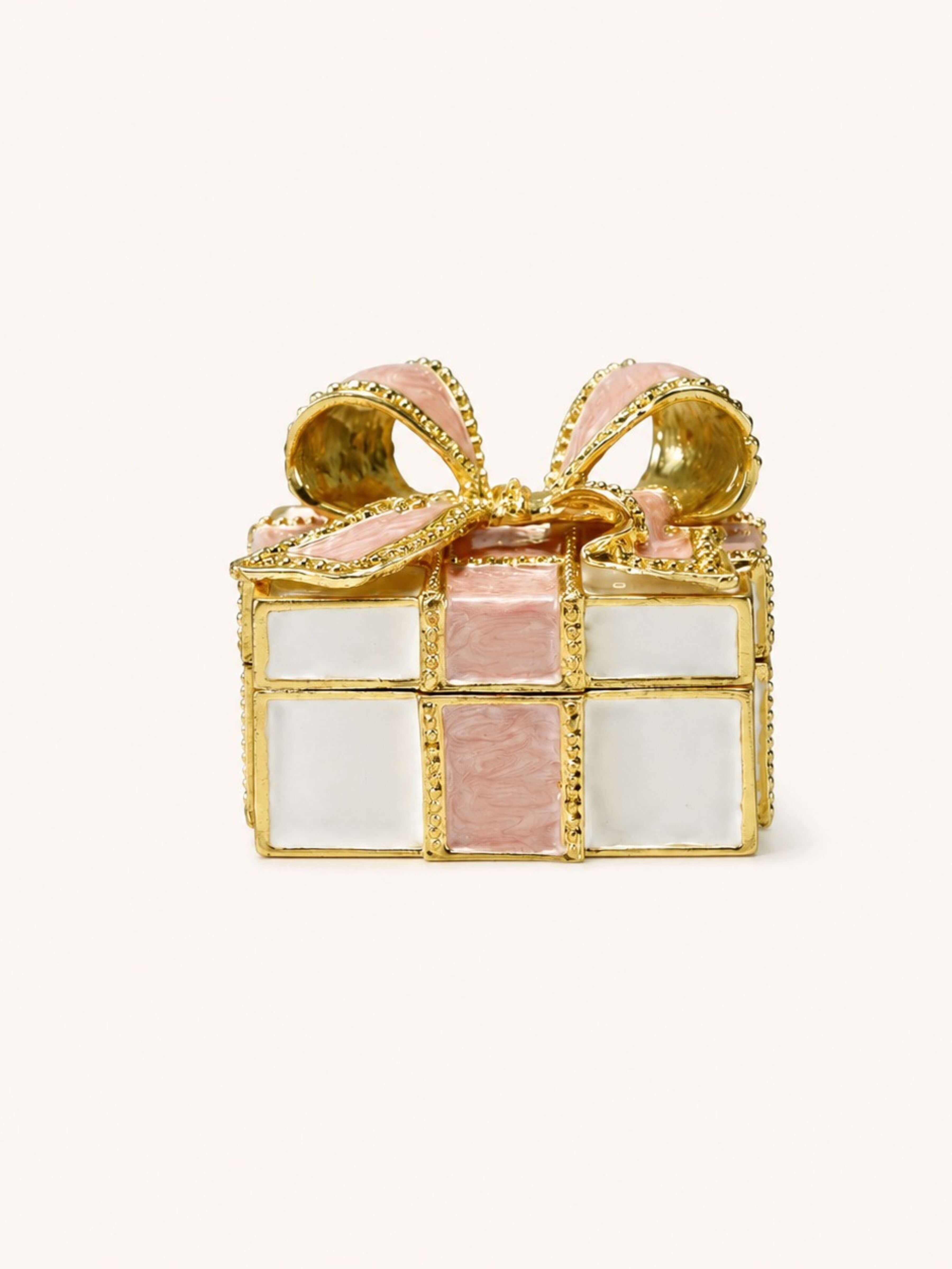 A gold-plated gift box ring with pink enamel panels and a pink ribbon bow, set against a plain off-white background.