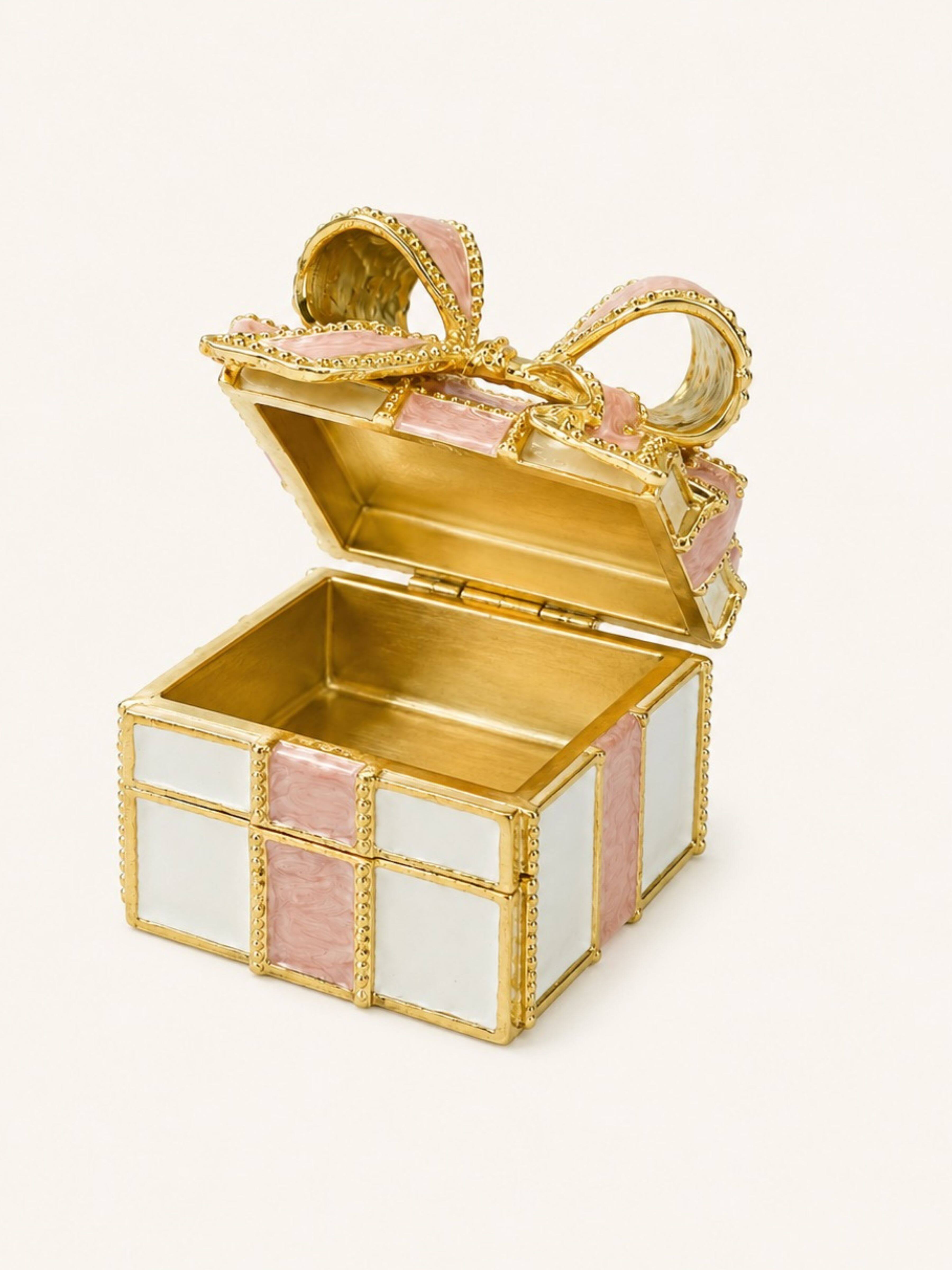 A small decorative gift box in gold-tone metal with pink and white enamel panels, shown open on a plain light background.
