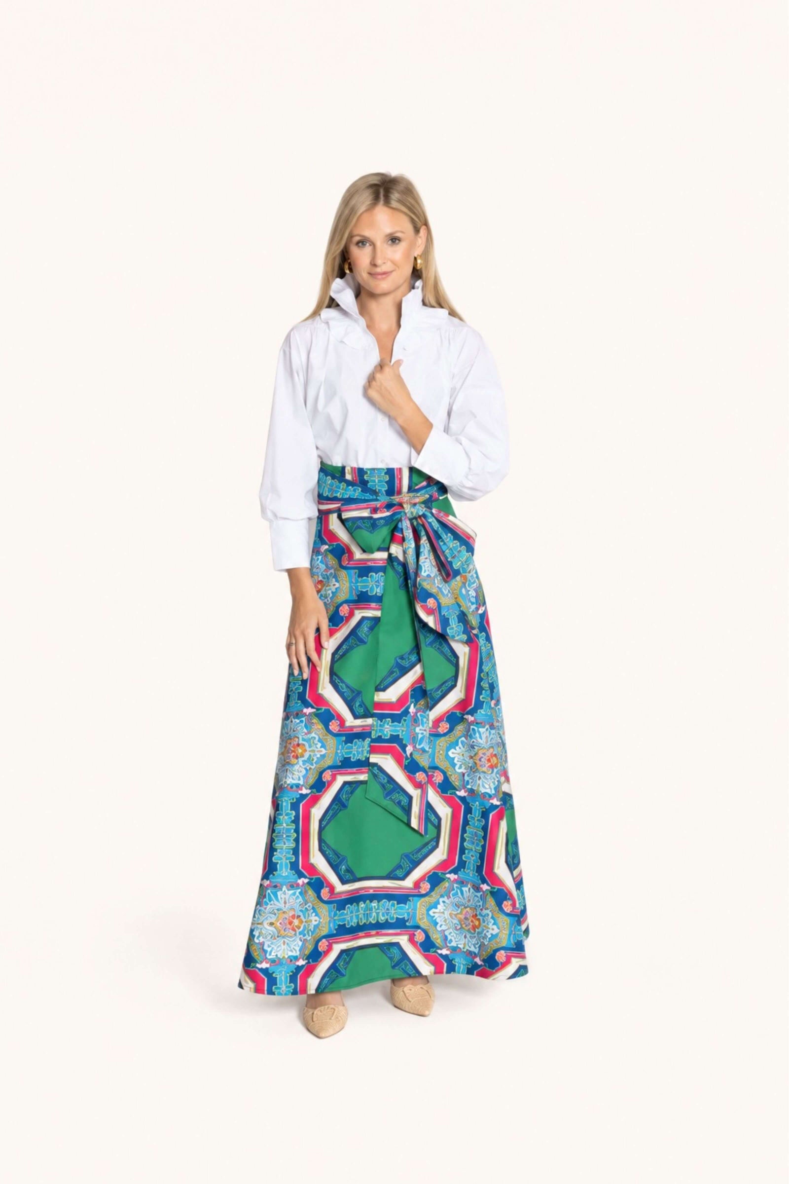 A woman modeling a long white button-up shirt and a high-waisted, tie-waist maxi skirt with a vibrant green, blue, pink, and white geometric pattern, set against a solid off-white background.