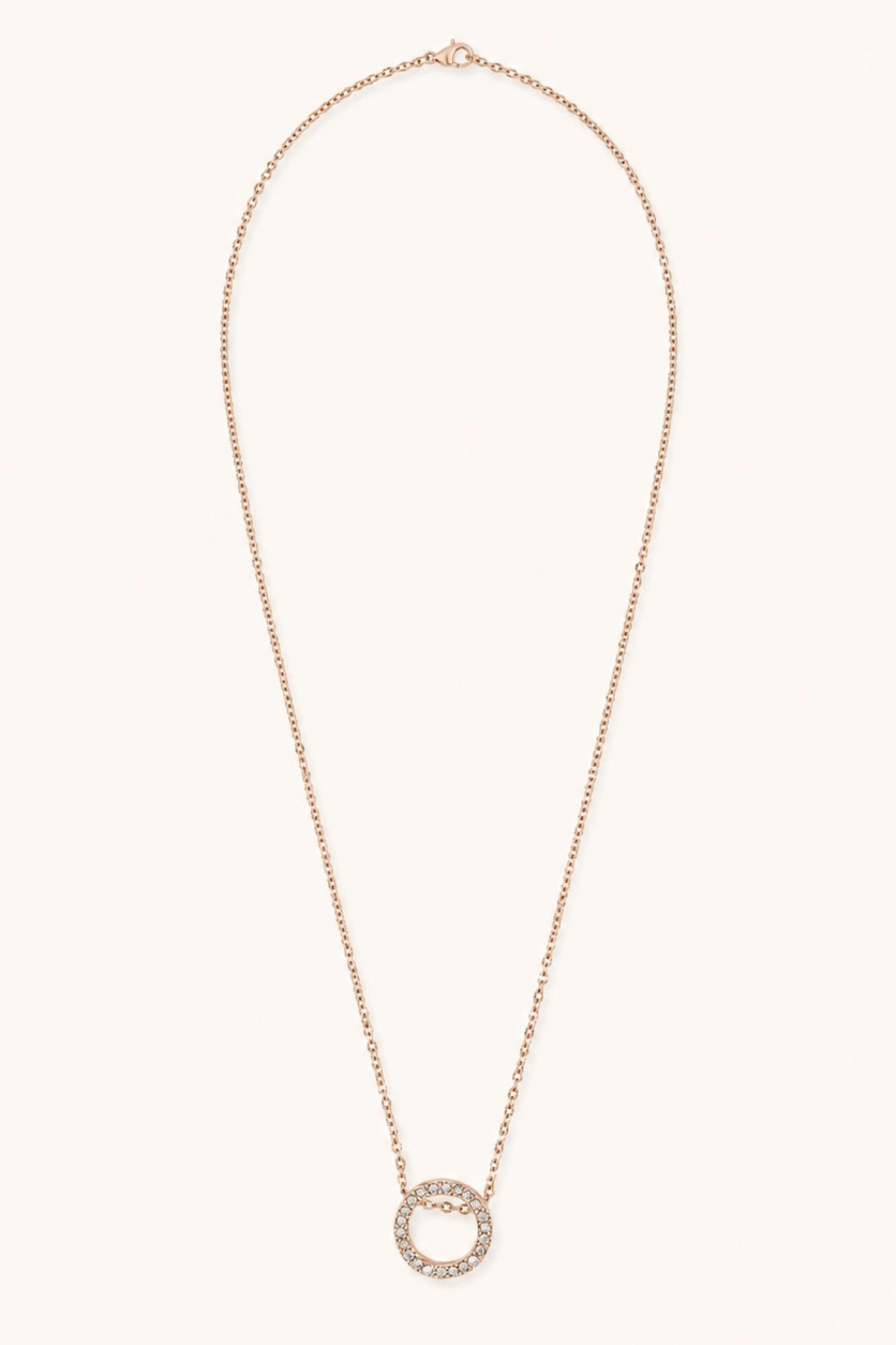 A delicate rose gold chain necklace featuring a circular pendant encrusted with small clear stones, displayed against a solid off-white background.
