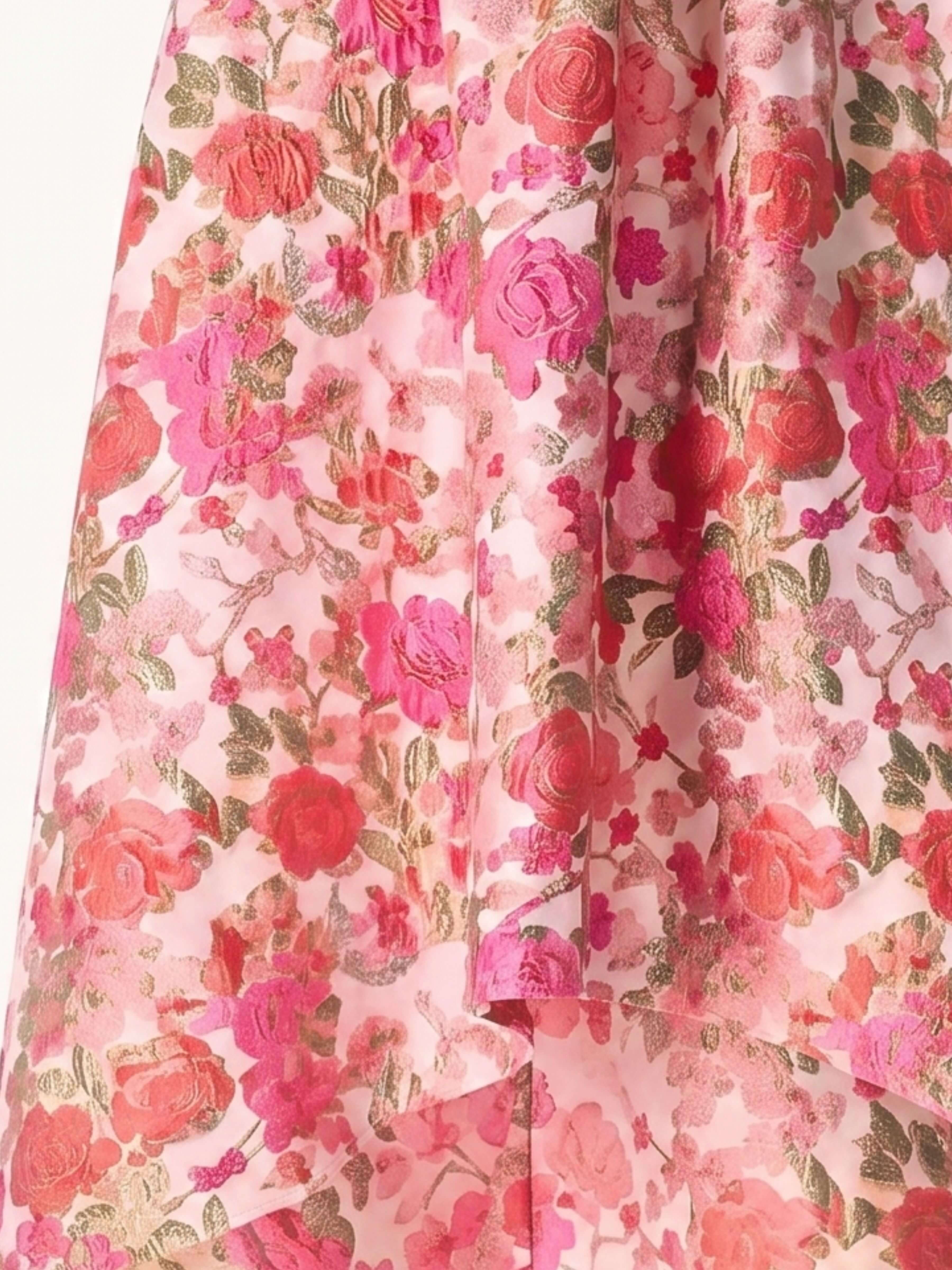 A close-up of a pink floral fabric with a metallic gold sheen, featuring roses and leaves in shades of pink, red, and gold.