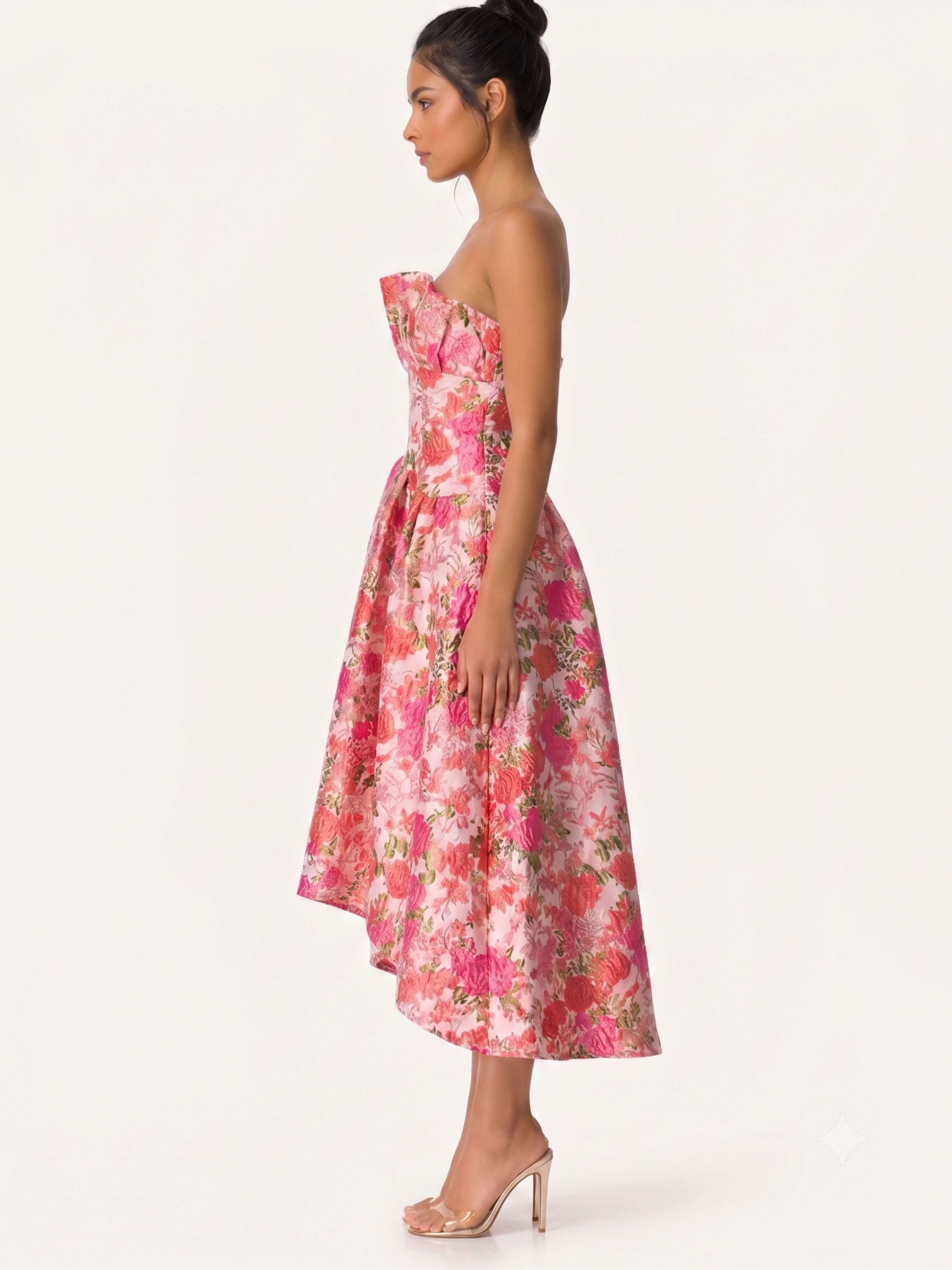 A woman modeling a strapless pink floral midi dress with a fitted bodice and flared skirt, shown in side profile against a plain light background.