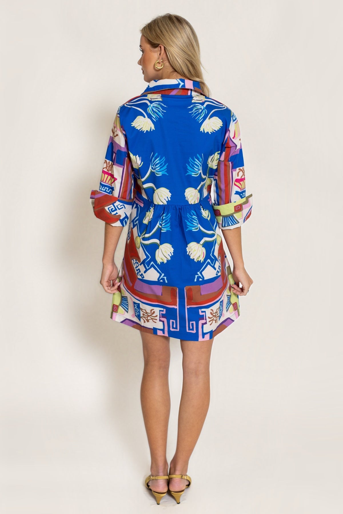 Back view of the Sapphire Blythe Empire Dress Short showing the full print and cuffed sleeves, on a warm neutral studio background.