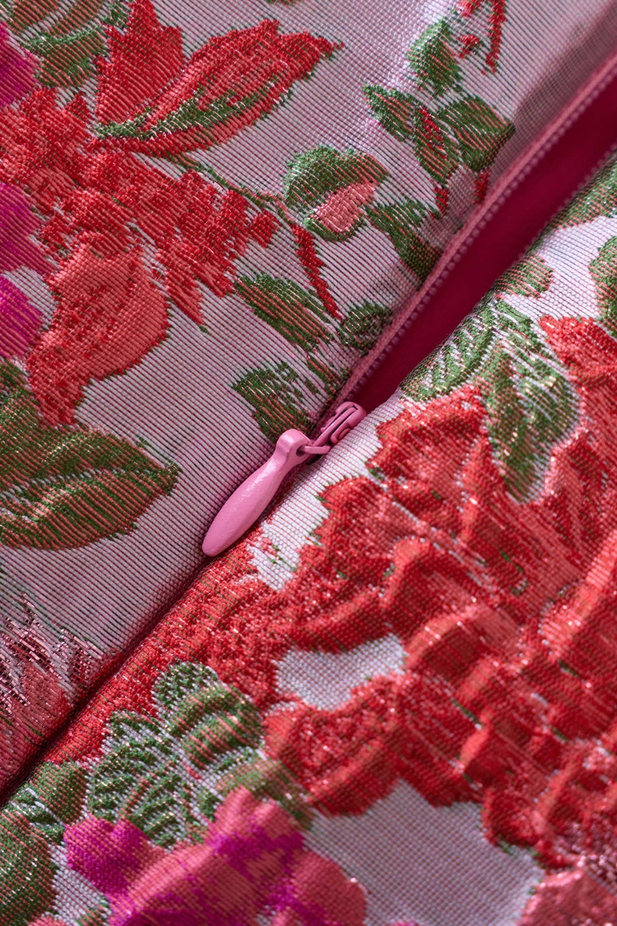 Close-up of the raised floral jacquard on The Garden Party Dress, red and pink roses with green leaves woven into the fabric, with the back zipper pull.
