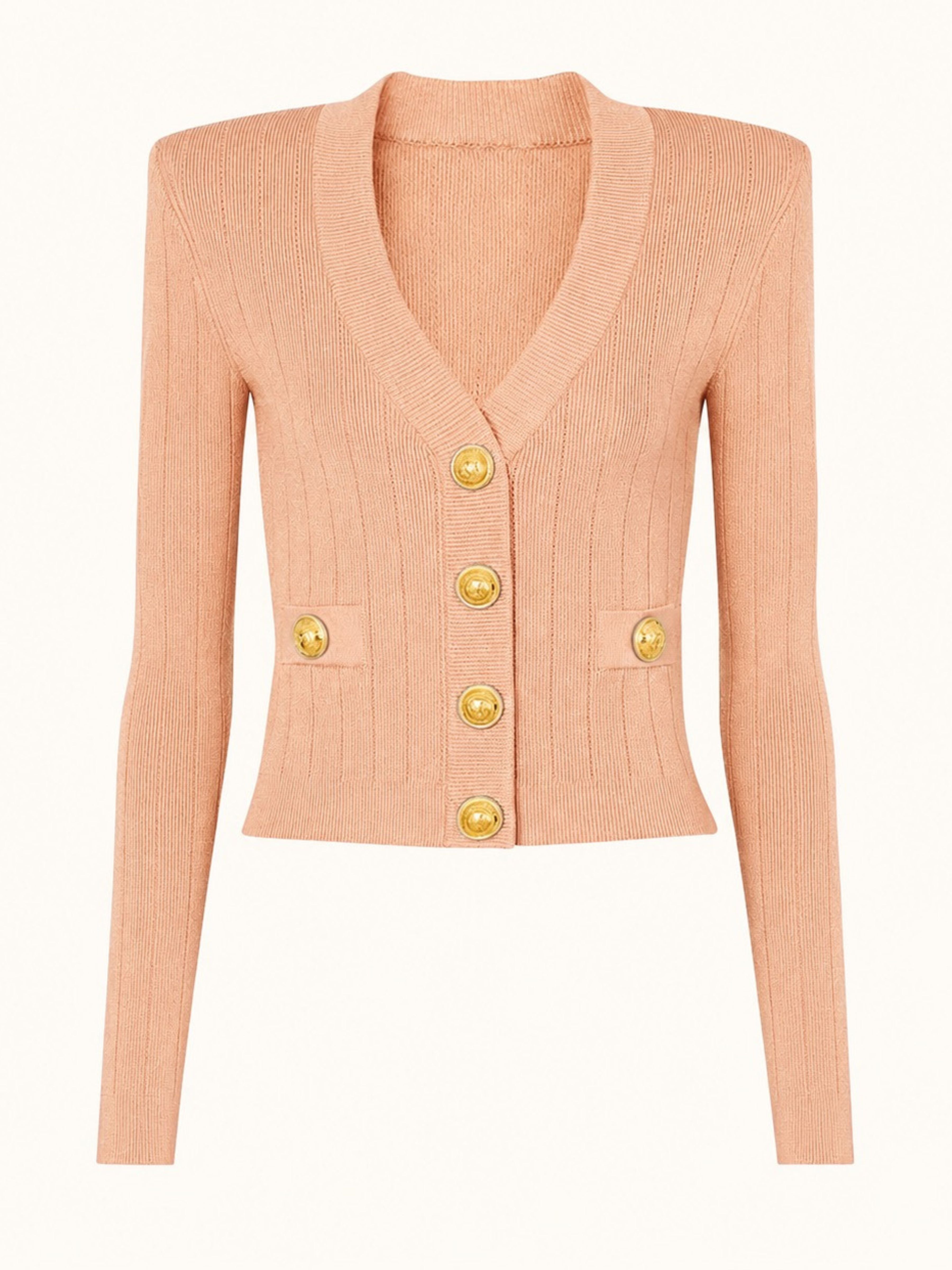 A cropped, long-sleeve ribbed knit cardigan in a soft peach-pink color, featuring gold-tone buttons down the front and two matching gold buttons on the chest pockets, shown against a plain white background.