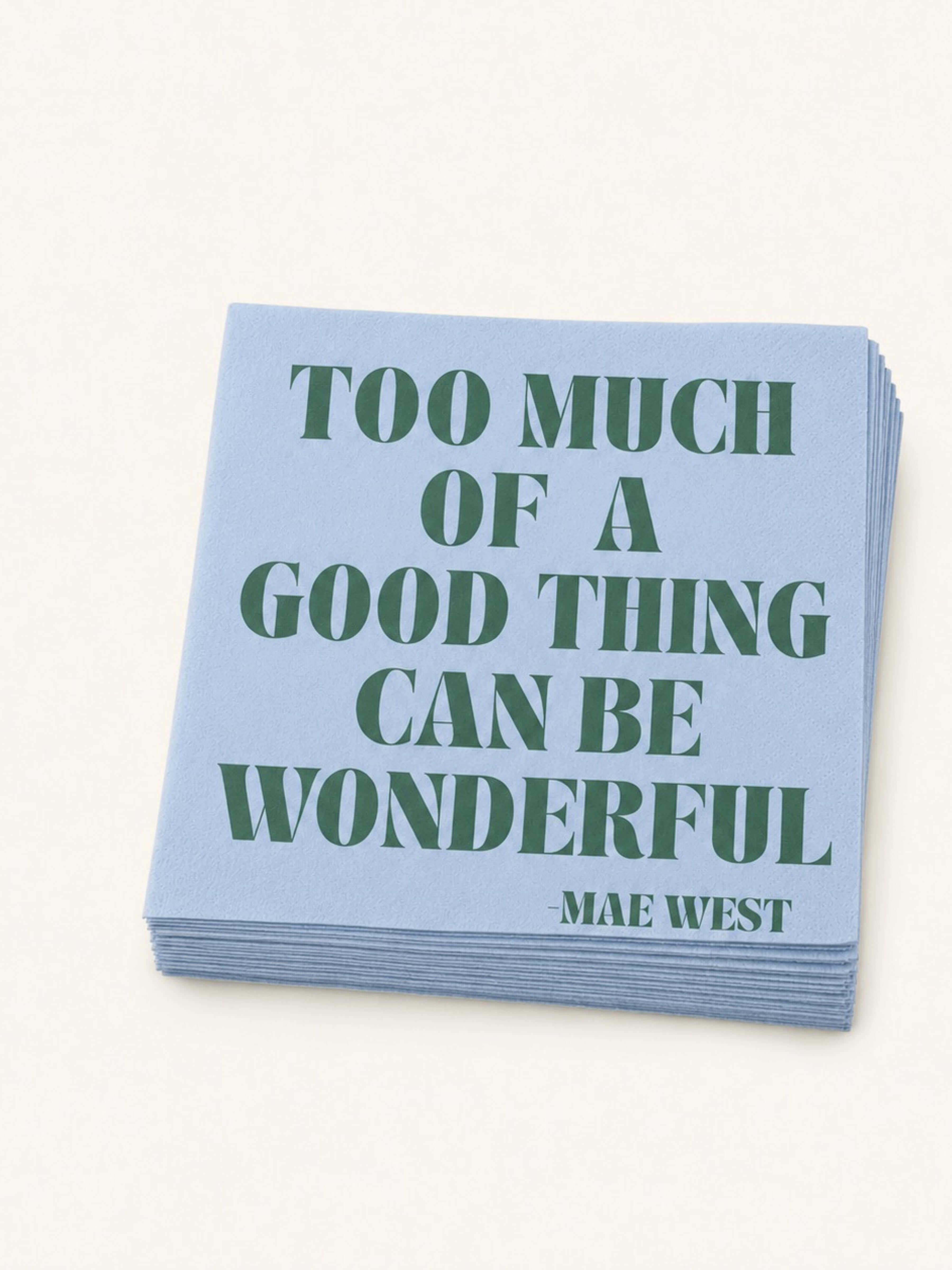 A stack of light blue paper napkins featuring the quote 'TOO MUCH OF A GOOD THING CAN BE WONDERFUL -MAE WEST' printed in dark green serif lettering, set against a solid off-white background.